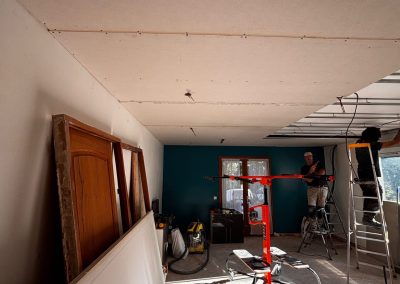 Installation du placo au plafond par les artisans AMT, avec lève-plaque et escabeau visibles sur le chantier.