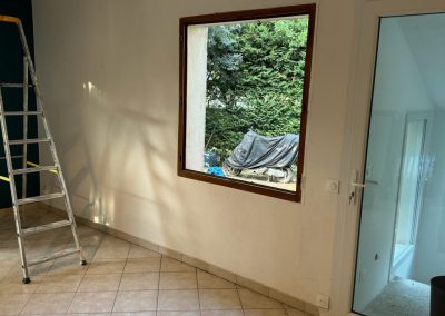 Vue de la fenêtre avant sa démolition, prête à être remplacée par une baie vitrée, avec l'encadrement encore en place.