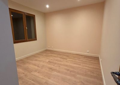 Chambre rénovée avec murs blancs et mur du fond peint en rose pâle, plafond équipé de spots LED, et carrelage imitation parquet bois au sol, parfait pour une chambre d'enfant.