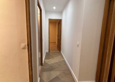 Couloir rénové par AMT Agence Multi Travaux, avec un grand carreau moderne au sol, des murs blancs épurés, et un éclairage plafond avec des spots LED apportant une lumière fonctionnelle et élégante.