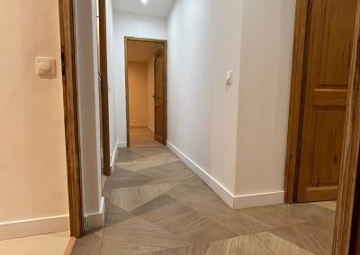 Couloir rénové par AMT Agence Multi Travaux, avec un grand carreau moderne au sol, des murs blancs épurés, et un éclairage plafond avec des spots LED apportant une lumière fonctionnelle et élégante.